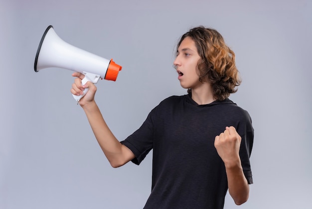 Guy with long hair in black t-shirt speaks through loudspeaker on white wall