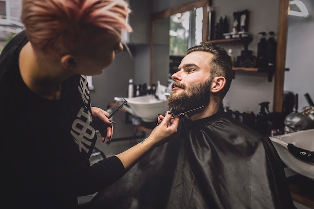 Hairdresser cutting beard of client