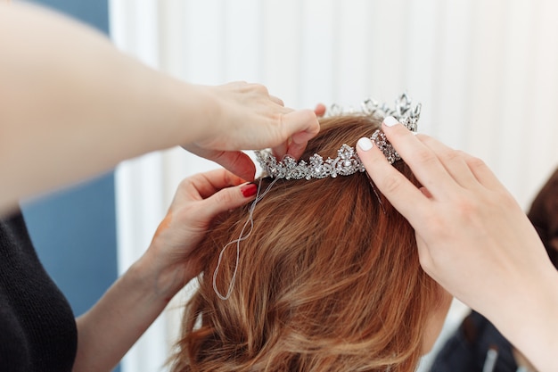 hairdresser makes models hairstyle for bride, putting on tiara crown.