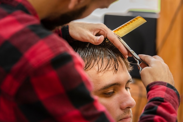 Free photo hairdresser trimming a young man with scissors