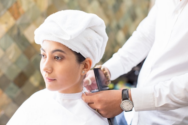 Hairdresser tying cape on serious female client