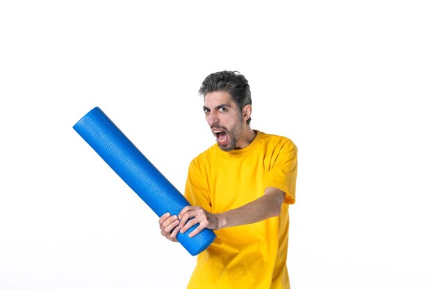 Half body shot of angry young man in yellow shirt and holding folded blue mat on white surface