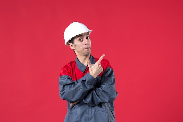 Free Photo half body shot of young builder in uniform wearing hard hat pointing up on isolated red wall