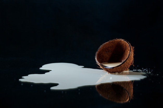 Free photo half of coconut with milk over black background.