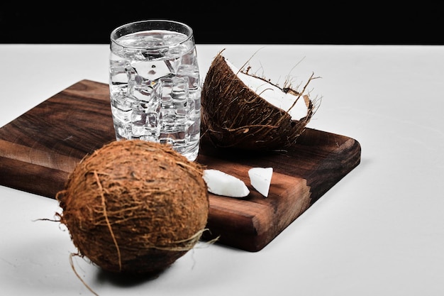 Free Photo half cut coconut on wooden board and glass of water with ice.