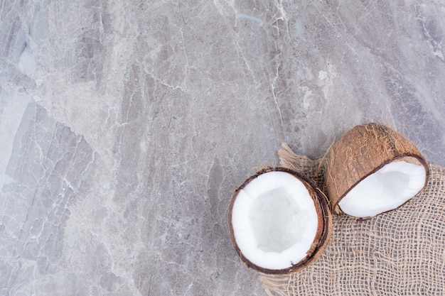 Free photo half cut coconuts with burlap on stone surface.