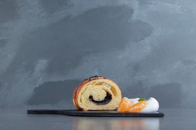 Free Photo half-cut croissant with tangerine slices on black cutting board.