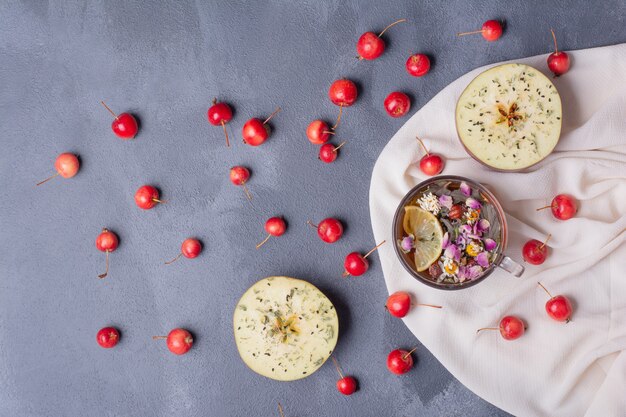 Half cut fruit, cherries and glass of juice with lemon slice and flowers on blue with tablecloth