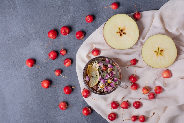 Half cut fruit, cherries and glass of juice with lemon slice and flowers on blue with tablecloth