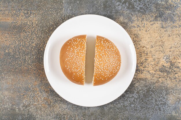 Half cut tasty bun with sesame seeds on white plate.