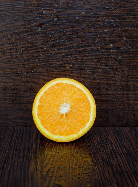 Half of fresh orange on a wet dark wooden surface