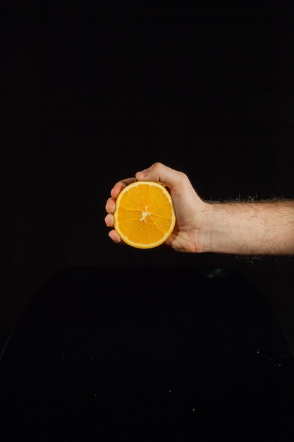 Half of a juicy orange in man's hand on black background