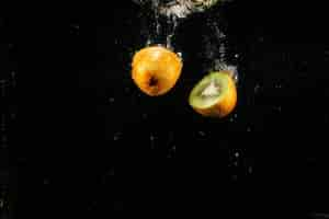 Free photo half of kiwi falling on black background