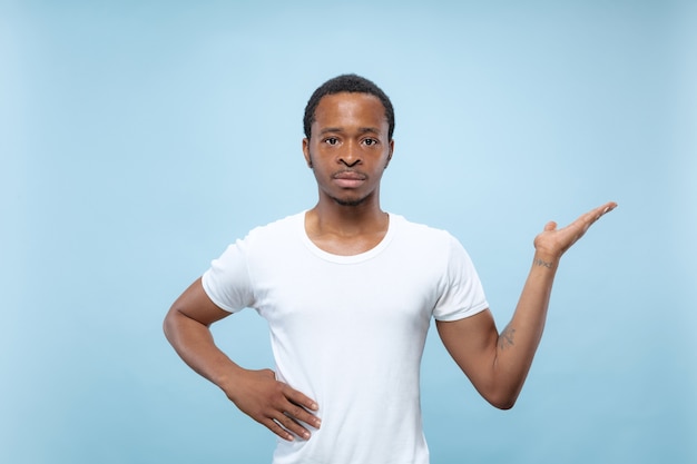 Half-length close up portrait of young african-american man in white shirt on blue space