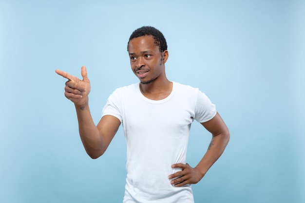 Half-length close up portrait of young african-american man in white shirt on blue space