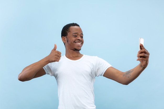 Half-length close up portrait of young african-american man in white shirt on blue space