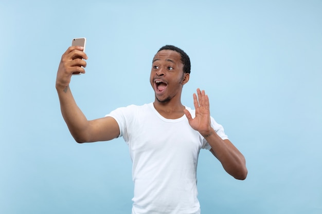 Half-length close up portrait of young african-american man in white shirt on blue space