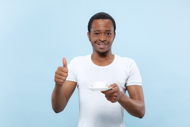 Half-length close up portrait of young african-american man in white shirt on blue space