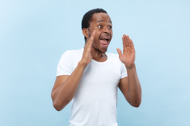 Half-length close up portrait of young african-american man in white shirt on blue space