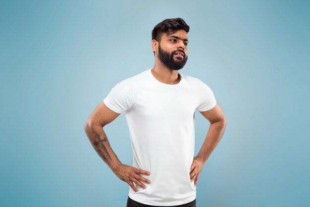 Half-length close up portrait of young hindoo man in white shirt on blue space