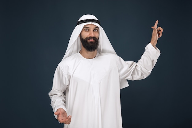 Half-length portrait of arabian saudi man on dark blue studio