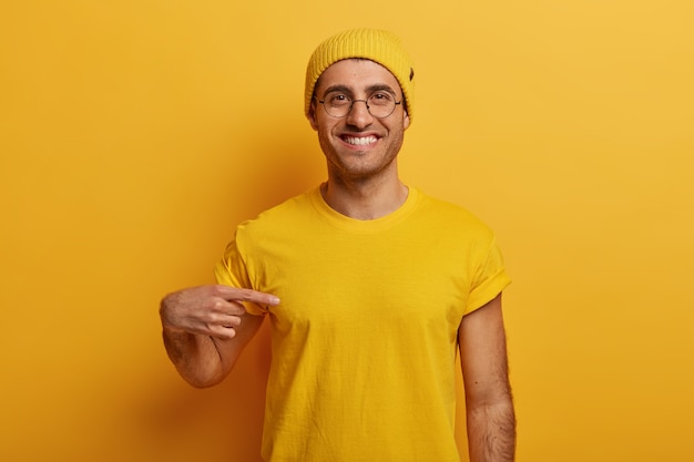 Free photo half length shot of cheerful man points at yellow t shirt, has glad expression, advertises new outfit, poses against bright background