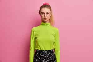 Free photo half length shot of confident serious schoolgirl ready for school, looks directly, has pony tail, wears green turtleneck and skirt