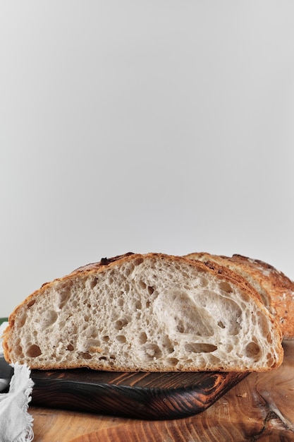 Free photo half a loaf of artisan sourdough bread on a cutting board closeup vertical frame on a light gray background with copy space