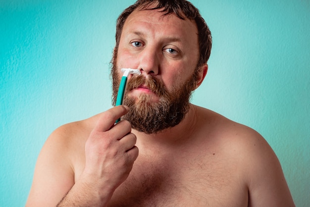 Half-naked Caucasian bearded man shaving with a serious face expression