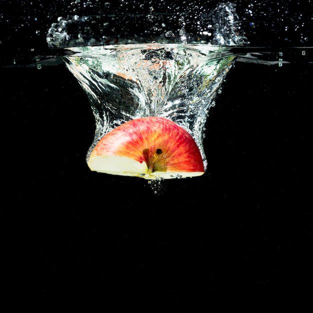 Half red apple falling into water with bubbles against black background