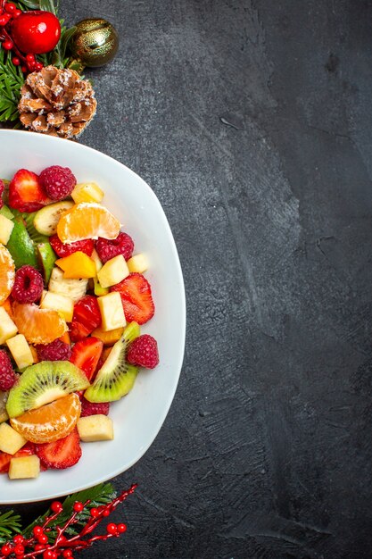 Half shot of collection of fresh fruits on dinner plate decoration accessories fir branches a on dark background