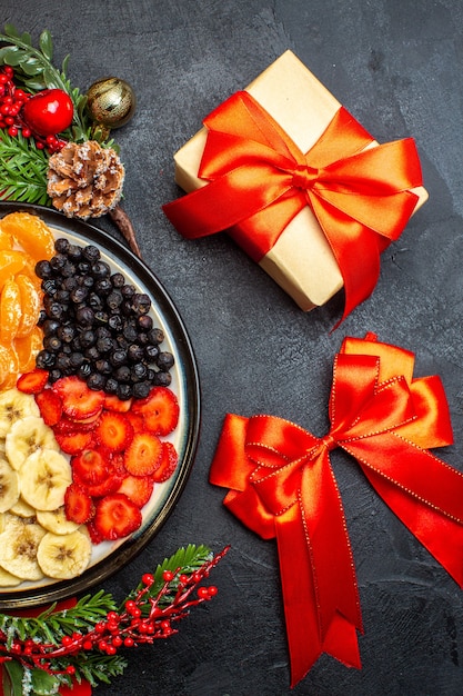 Half shot of collection of fresh fruits on dinner plate decoration accessories fir branches and numbers on a red napkin and red rbbon and gift