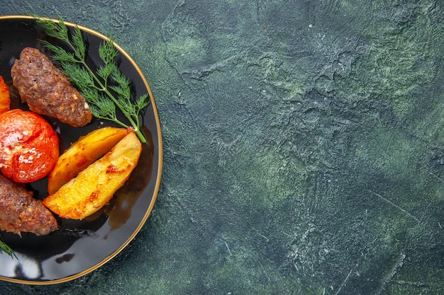 Free photo half shot of delicious meat cutlets baked with potatoes and tomatoes on a black plate on the right side on green black mixed color background