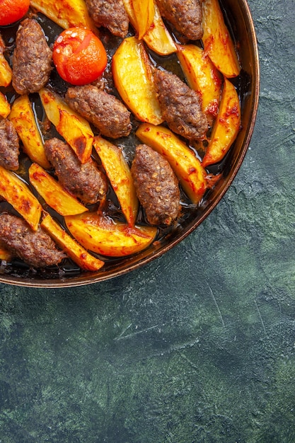 Half shot of delicious meat cutlets baked with potatoes and tomatoes on green and black mix color background in vertical view