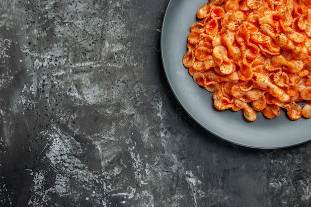 Half shot of delicious pasta meal on a black plate for dinner on dark table