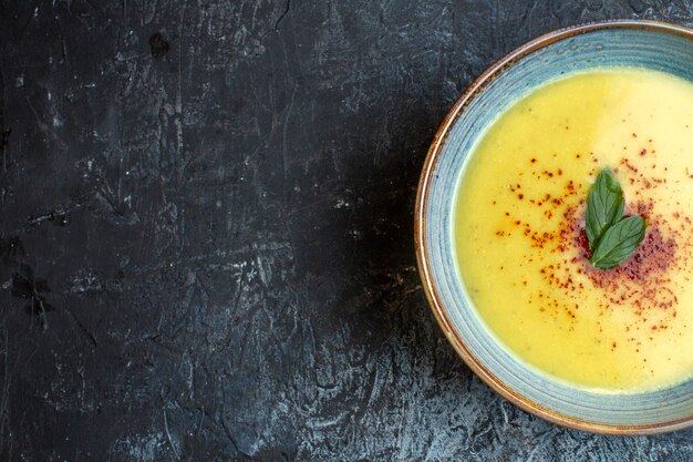 Half shot of delicious soup served with pepper and mint in a blue pot on the left side on dark background