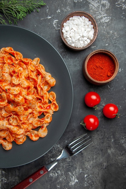 Free Photo half shot of easy pasta meal for dinner on a black plate and fork on different spices and tomatoes on a dark table