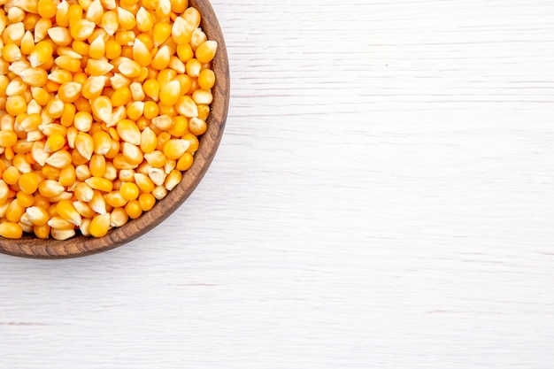 Half shot of fresh corn kernels in a brown bowl on white table