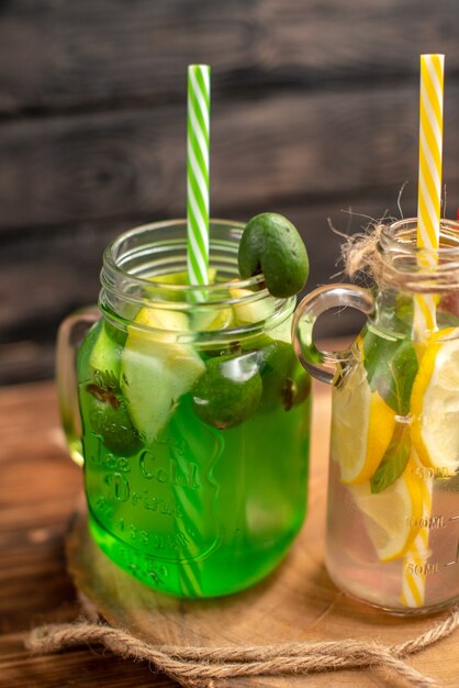 Half shot of natural organic fuit juices in bottles served with tubes on a wooden cutting board on a brown table