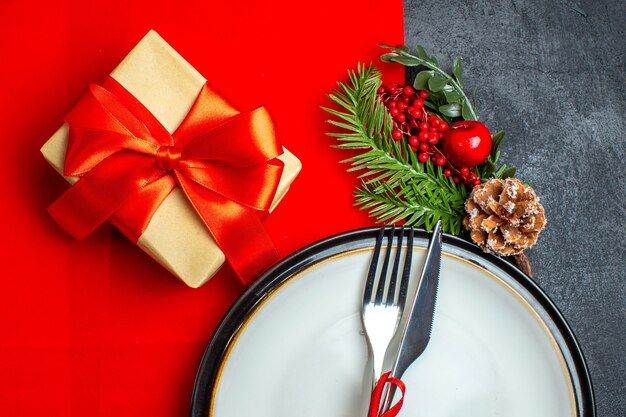 Half shot of New year background with cutlery set with red ribbon on a dinner plate decoration accessories fir branches next to a gift on a red napkin