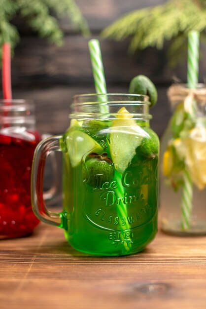 Half shot of organic fresh juices in bottles served with tubes and fruits on a brown wooden background