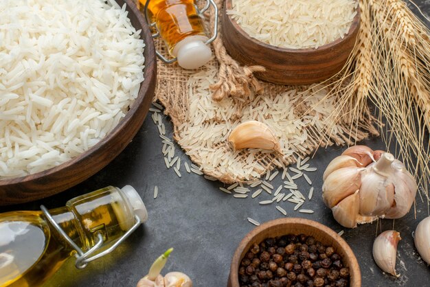 Half shot of perfect long rice brown bowls on nude color towel fallen oil bottles garlics peppers on dark background