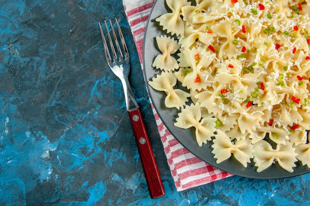 Free photo half shot of raw italian farfalle pasta on red stripped towel and cutlery set on the left side on blue table