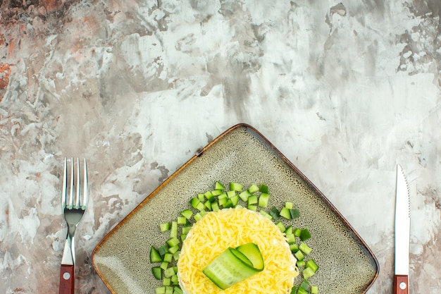 Half shot of tasty salad served with chopped cucumber and knife fork on mixed color background