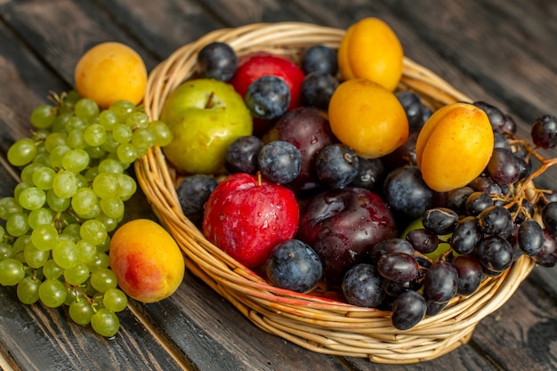 Half-top view basket with fruits mellow and sour fruits such as grapes apricots plums on the brown desk