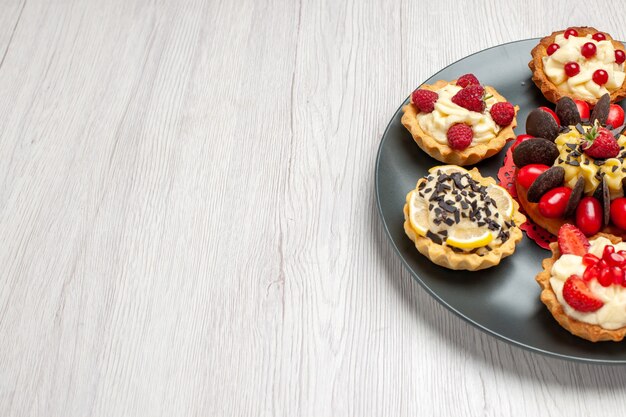 Half-top view chocolate cake rounded with berry tarts in the grey plate on the white wooden table with copy space