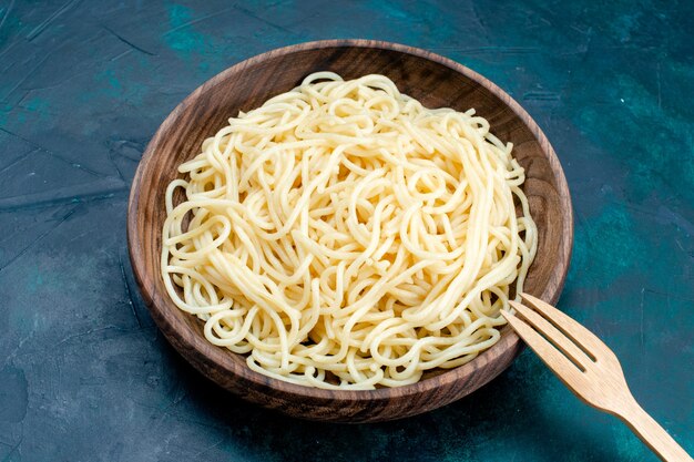 Half-top view cooked italian pasta inside round wooden plate on blue surface pasta italy food dinner dough meat