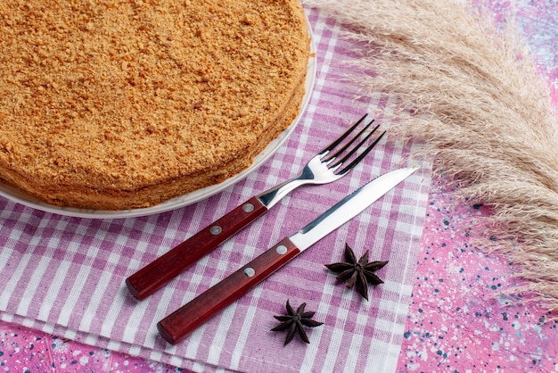 Half-top view delicious round cake inside plate with cutlery on the bright pink desk cake pie biscuit sweet bake