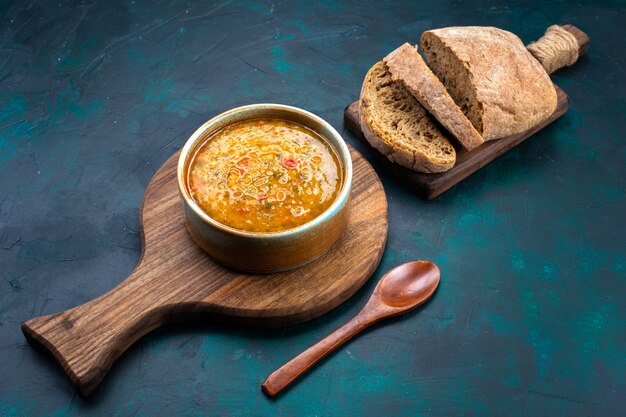 Half-top view delicious vegetable soup inside round plate with bread on the dark-blue desk.