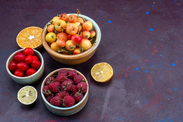 Half-top view of fresh fruits raspberries plums inside plates on dark surface